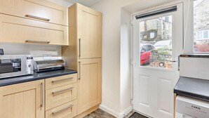 A compact kitchen with wooden cabinets, a built-in microwave, and a white door leading outside. - 2 Bed in Hexham (oc-50500) (Bellingham)