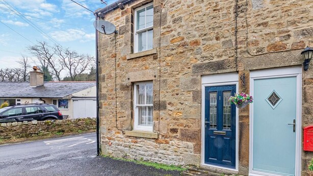 A stone building with a blue door, a satellite dish, and a stone wall. - 2 Bed in Hexham (oc-50500) (Bellingham)