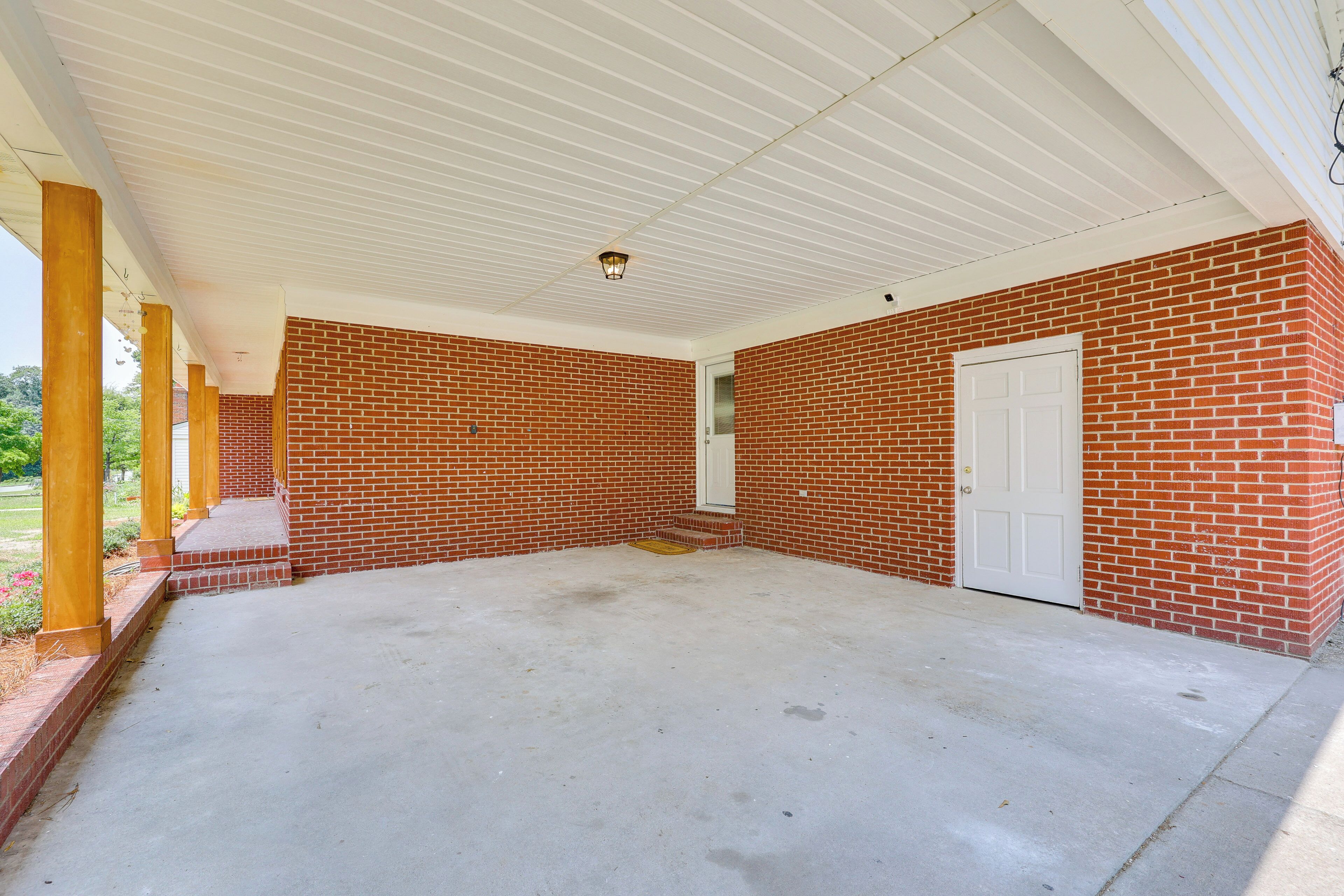 A covered patio area with a brick wall, a white door, and a concrete floor.