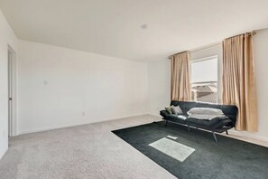 Ett rum med en svart soffa, beige gardiner, ett fönster och en grå matta.