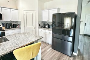 A modern kitchen with white cabinets, a granite countertop, a stainless steel refrigerator, and a yellow chair.