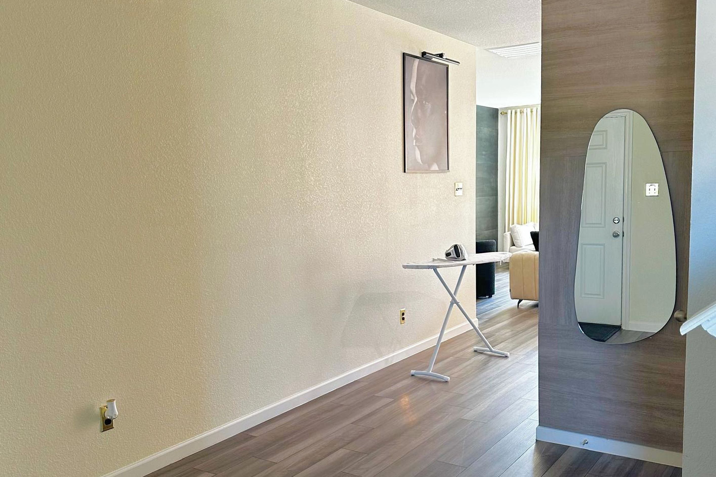 Une chambre d’hôtel moderne avec un plancher en bois, une petite table avec une chaise, un grand miroir et une porte décorée avec un motif de planche de surf.