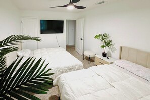 A bedroom with two beds, a ceiling fan, a TV, a potted plant, and a door leading to another room.
