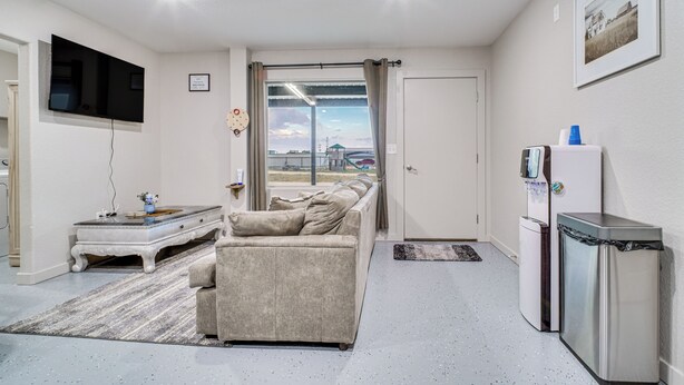 A modern living room with a sofa, a flat-screen TV, a small table, a refrigerator, and a window with curtains. - Family Fun! Quaint Seminole Home w/ Grill & Patio (Seminole)