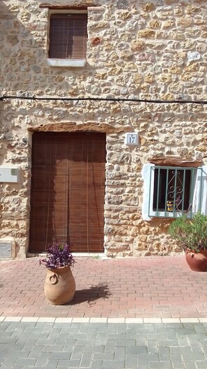 Un edificio de piedra con una puerta de madera grande, una ventana pequeña con barrotes de metal y una planta en maceta en el suelo.