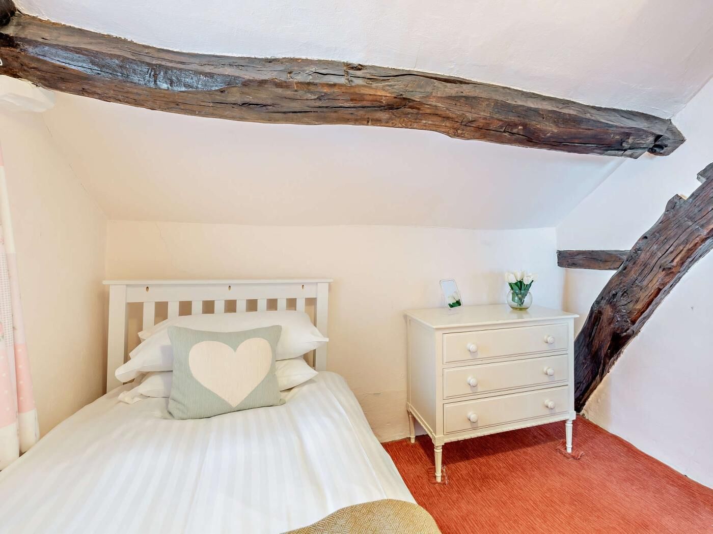 A bedroom with a white bed, a dresser, and exposed wooden beams.