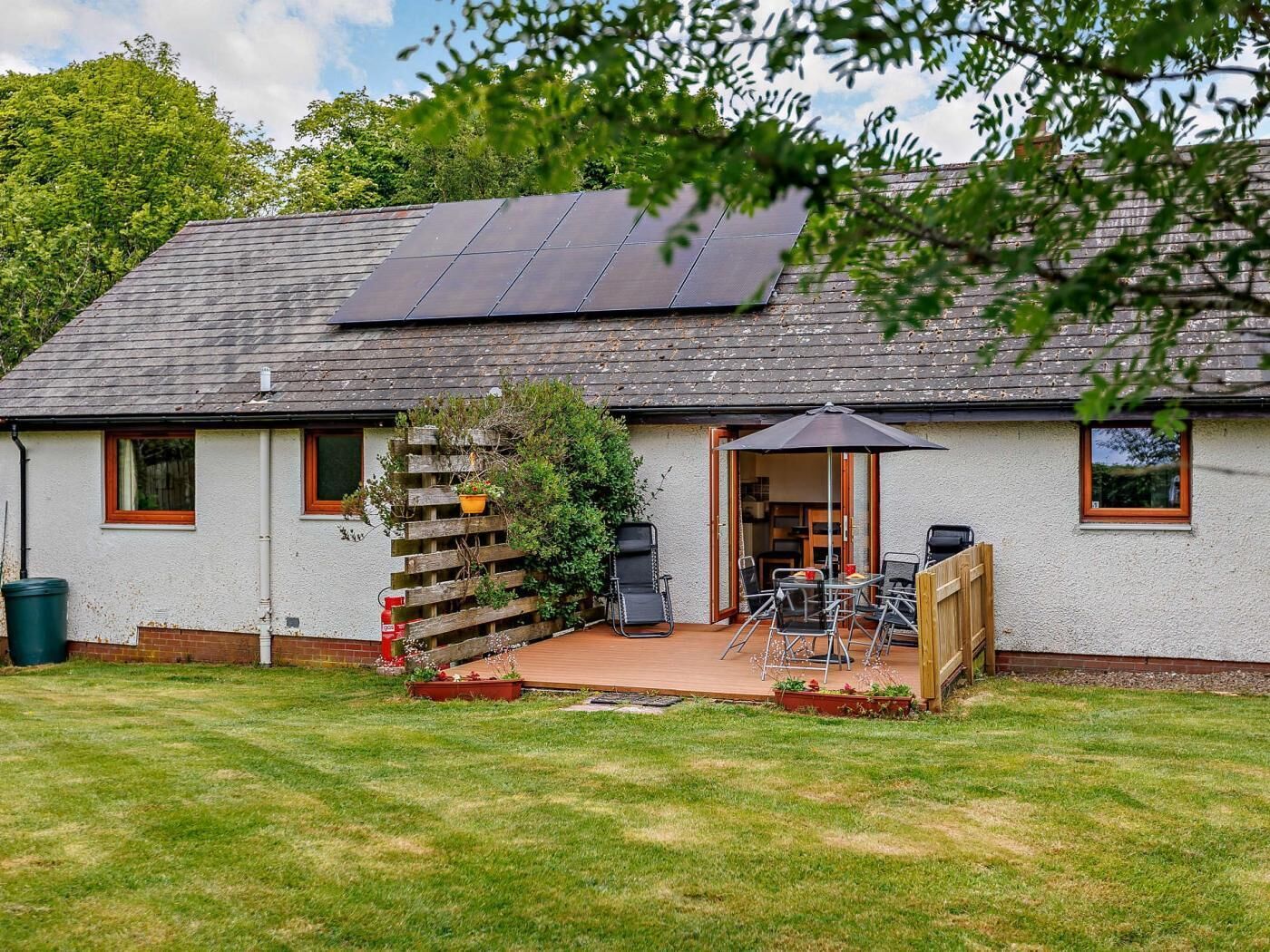 Una casa con techo de paneles solares, un patio con mobiliario exterior y una cerca de madera.
