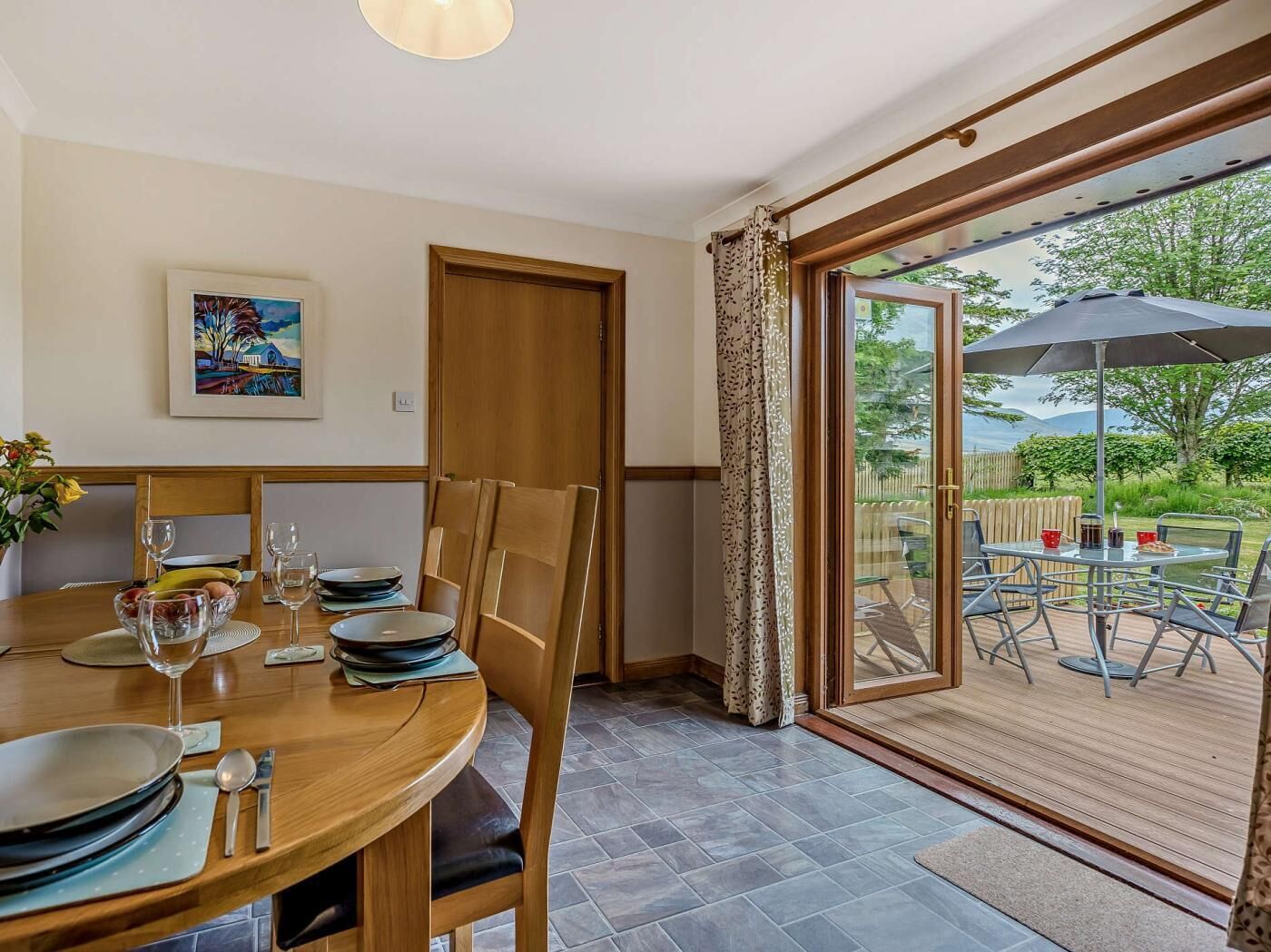 Un coin repas avec une table dressée pour quatre personnes, un tableau accroché au mur et une porte-fenêtre coulissante donnant sur une terrasse extérieure.