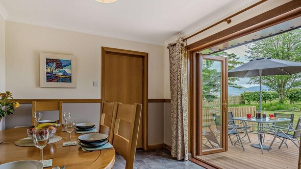A dining area with a table set for four, a painting on the wall, and a sliding glass door leading to an outdoor patio. - 3 Bed in Dunkeld (oc-50619) (Amulree)