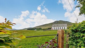 A rural landscape with a white building, possibly a house or chapel, surrounded by green fields and hills. - 3 Bed in Dunkeld (oc-50619) (Amulree)