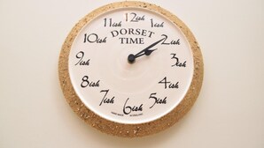 Et rundt vægur med en korkfod og en hvid urskive, der viser tiden i DORSET.