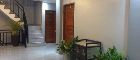Un pasillo con una escalera, una puerta de madera y plantas en macetas.
