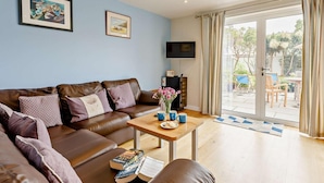 A living room with a brown leather sofa, a wooden coffee table, and a TV mounted on the wall. - 4 Bed in Bude (oc-50591) (Bude)