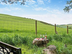 A grassy field with a wooden fence, a picnic table with food and drinks, and a bench. - 2 Bed in Mindrum (oc-50973) (Kilham)