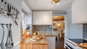 Une cuisine moderne avec un îlot central en bois, des ustensiles de cuisine suspendus et une vue sur la salle à manger.