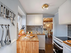 A modern kitchen with a wooden island, hanging utensils, and a view into the dining area. - 2 Bed in Colwyn Bay (oc-50933) (Eglwysbach)