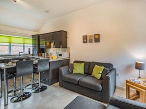 Eine moderne Küche mit Essbereich, ein graues Sofa mit grünen Kissen und ein kleiner Holztisch mit Lampe.