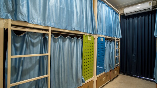 A room with bunk beds, each with a number label, and a large window covered by curtains. - The Hobohomes Varanasi - Hostel & Private Rooms Near Sarnath (Varanasi)