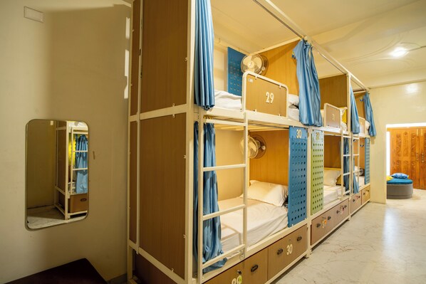 A dormitory room with bunk beds, a mirror, and a wardrobe.