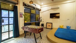 A room with a foosball table, a bed, a television, and a window with curtains.