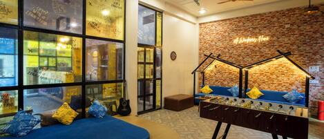 A cozy room with a brick wall, a sofa, a foosball table, and a window with travel-themed decorations.