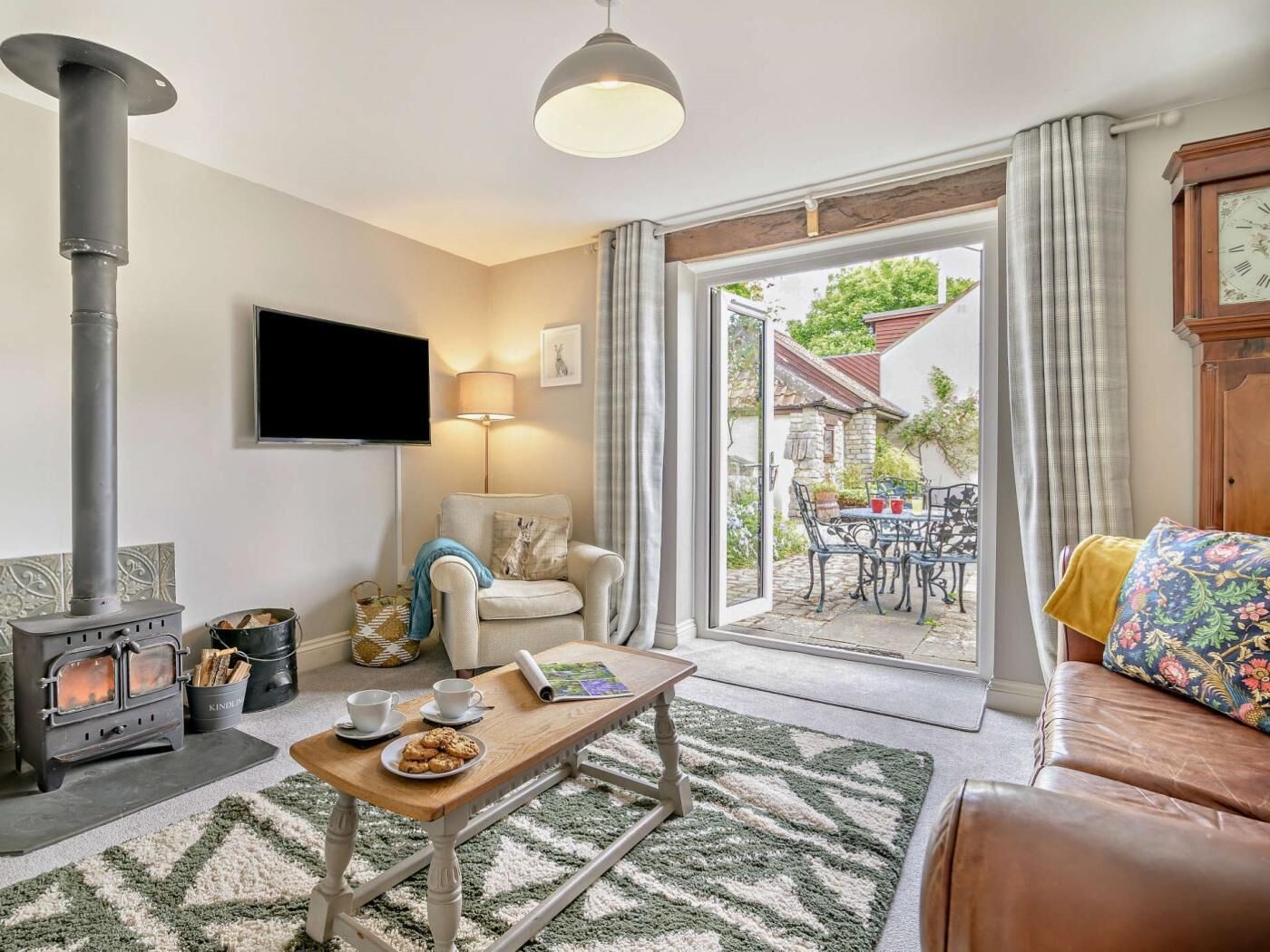 Ein gemütliches Wohnzimmer mit Kamin, Fernseher, einer Couch und einem Essbereich mit Gartenmöbeln.