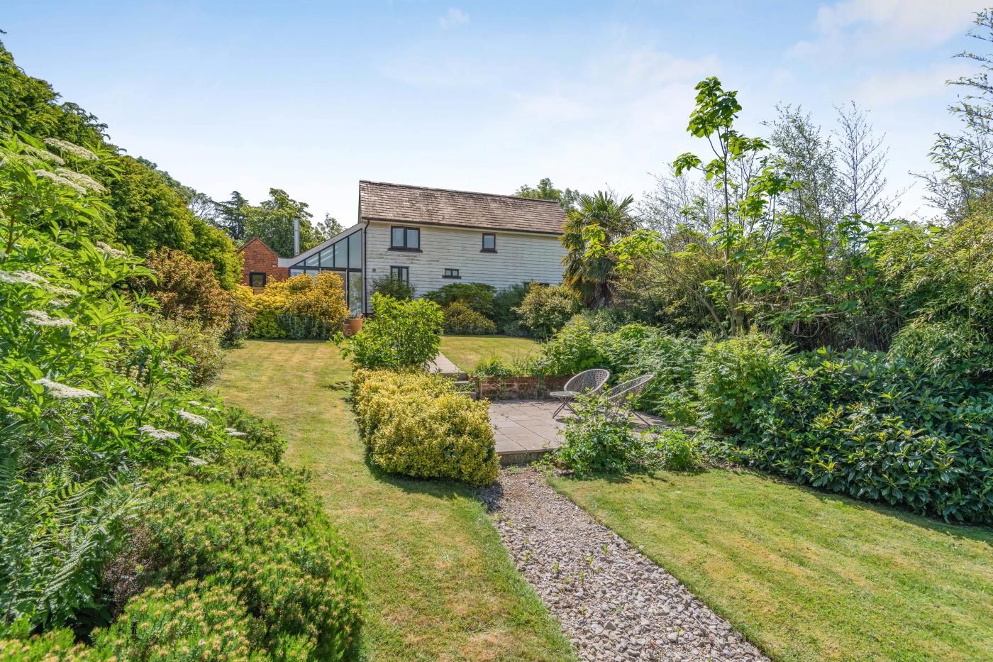 A house with a well-maintained garden, a patio with outdoor furniture, and a clear sky.