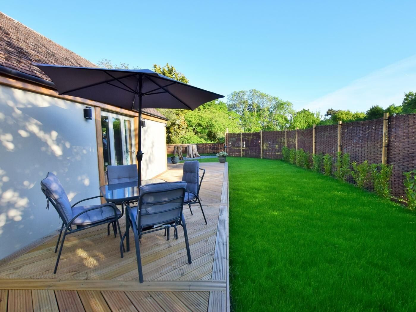 Una terraza con mobiliario exterior, un espacio cubierto y un césped cuidado.