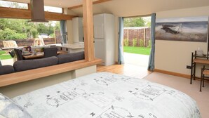 A modern kitchen with a dining area, a large bed with a detailed duvet, and a view of the garden. - 1 Bed in Lymington (oc-50723) (Sway)