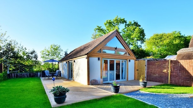 A small house with a thatched roof, a patio, and a garden. - 1 Bed in Lymington (oc-50723) (Sway)