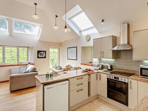 A modern kitchen with a skylight, a dishwasher, an oven, and a dining area with a sofa. - 2 Bed in Fort William (oc-50975) (Strone)
