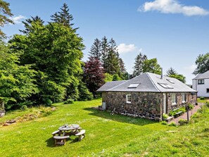 A stone cottage with a sloped roof, surrounded by lush greenery and trees. - 2 Bed in Fort William (oc-50975) (Strone)