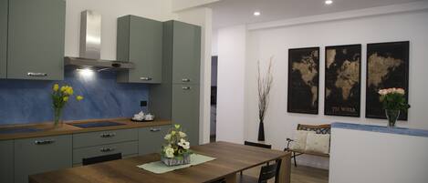 A modern kitchen with green cabinets, a wooden dining table, and a bench. There are three framed world maps on the wall.