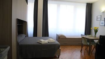 Une chambre d’hôtel comprenant un lit, un bureau, une chaise, une petite table, une fenêtre avec des rideaux et un téléviseur fixé au mur.