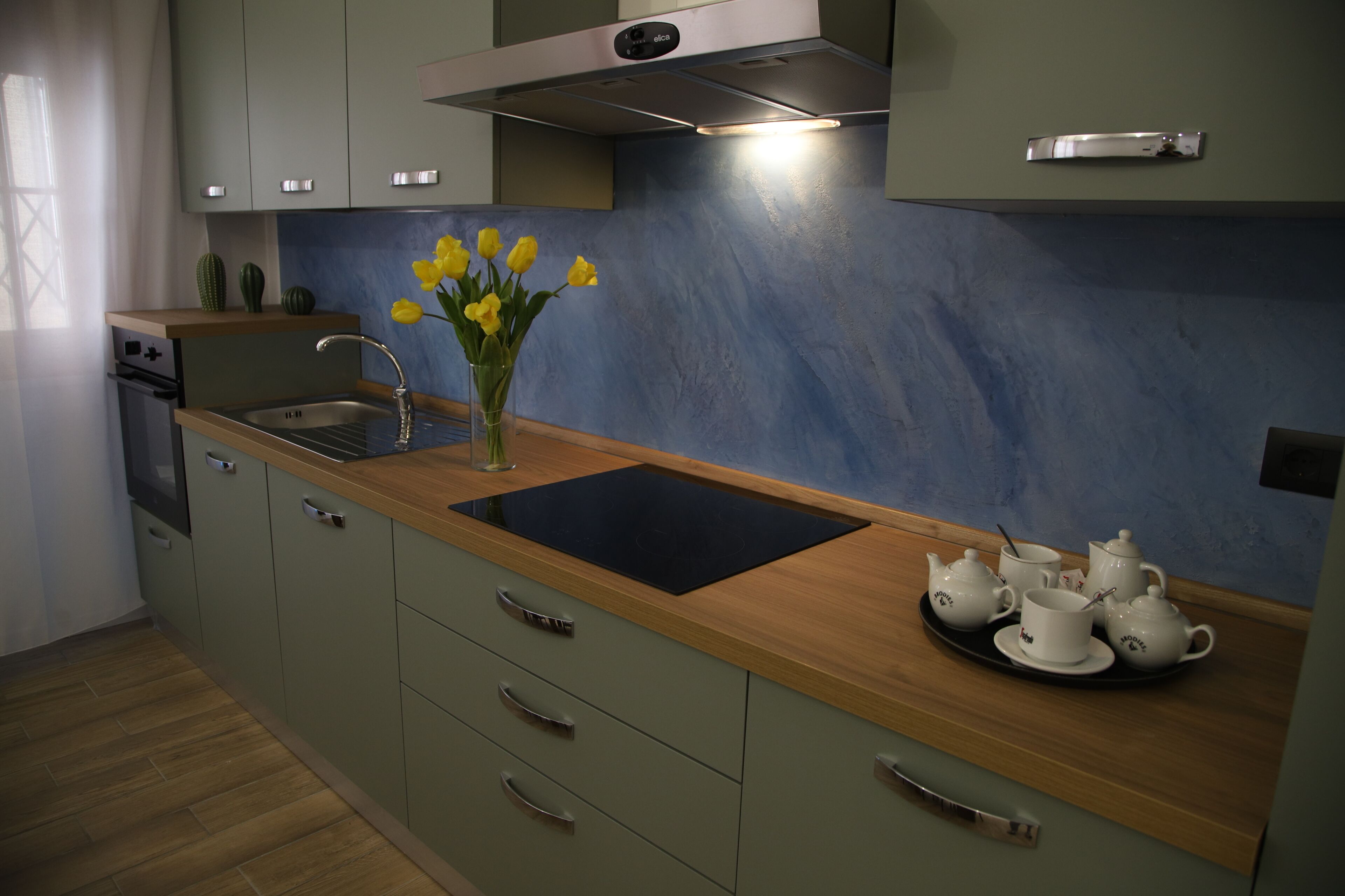 Una cocina moderna con encimera de madera, un lavamanos y una bandeja con teteras y tazas.