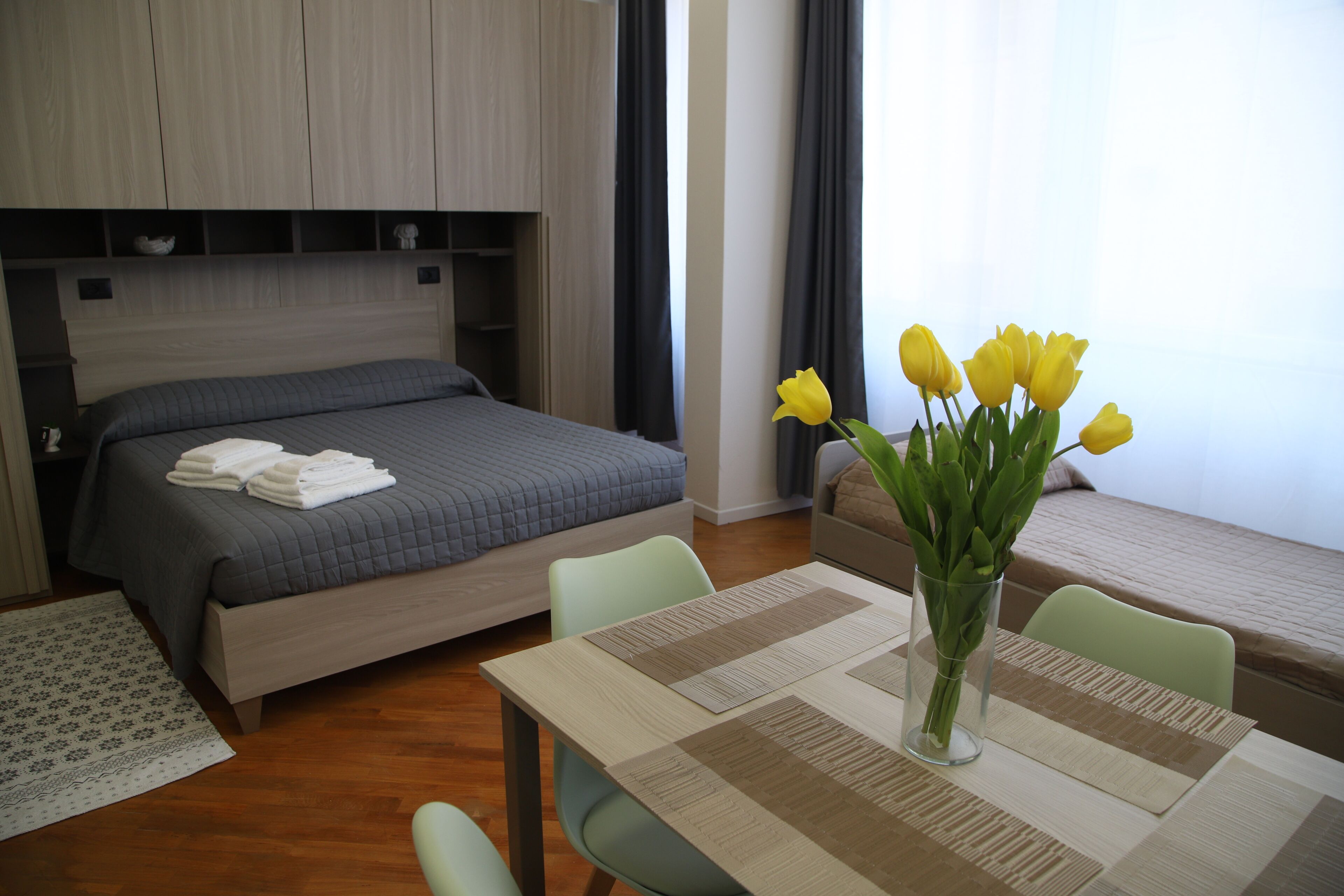 Una camera d'albergo con un letto, un tavolo da pranzo con un vaso di fiori e una finestra con tende.