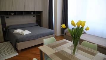 Una camera d'albergo con un letto, un tavolo da pranzo con un vaso di fiori e una finestra con tende.
