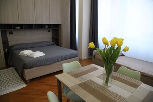 A hotel room with a bed, a dining table with a vase of flowers, and a window with curtains.