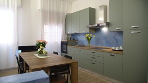 A modern kitchen with green cabinets, a wooden dining table, and a vase of flowers. - LA TORRETTA (Savona)