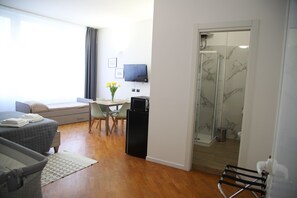 A modern hotel room with a bed, a desk, a chair, a TV, a shower, and a view of the outdoors.