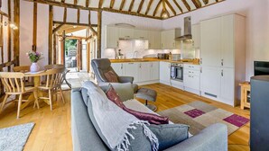 A rustic interior with exposed wooden beams, a dining area with wooden chairs, a grey sofa, and a kitchen with white cabinets. - 1 Bed in Dunmow (oc-51222) (Thaxted)