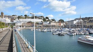 A marina with boats docked, a promenade with a railing, and buildings in the background. - 2 Bed in Torquay (oc-51143) (Torquay)