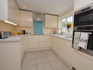 A modern kitchen with white cabinets, a stainless steel oven, and a window with a view of greenery. - 1 Bed in Sherborne (oc-51018) (Thornford)