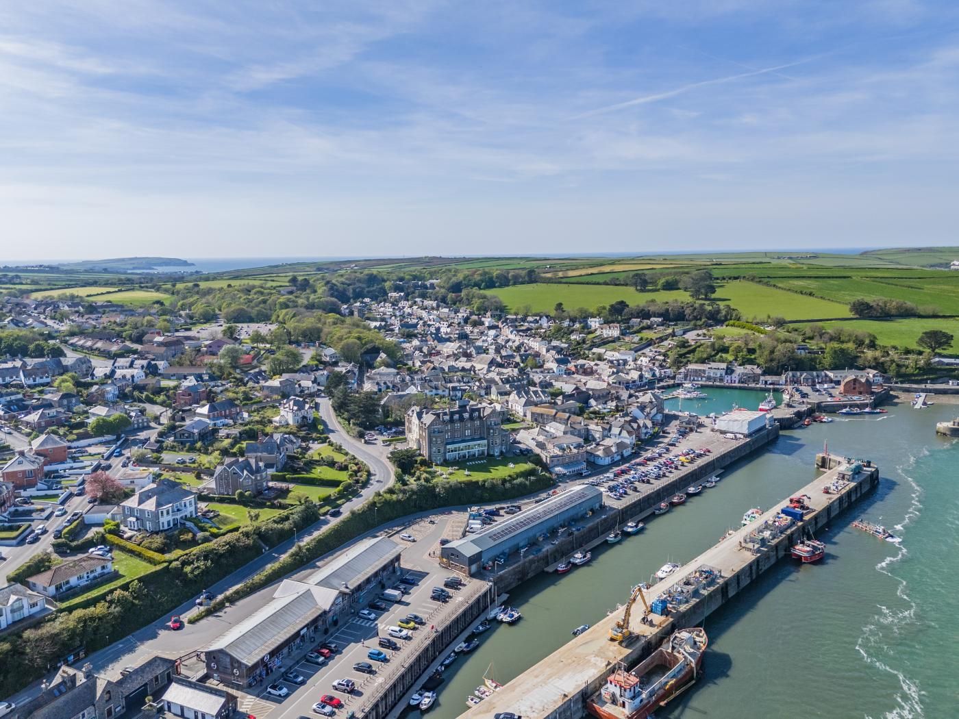 An aerial view of a coastal town with a marina, residential areas, and a prominent building with a large parking lot.