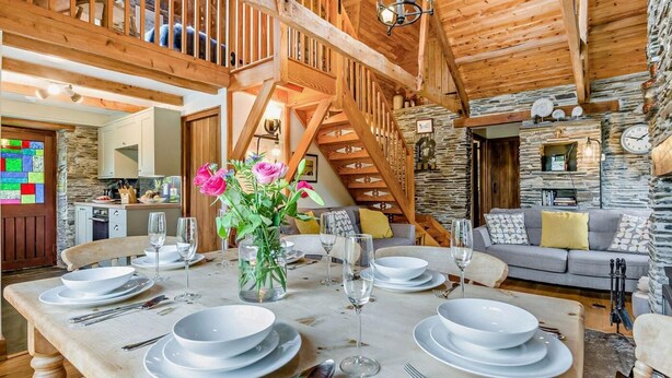 A dining area with a wooden table set for four, a staircase, and a stone wall with a clock. - 3 Bed in Padstow (oc-51214) (Padstow)