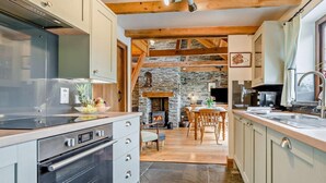 A modern kitchen with a stone fireplace, wooden beams, and a dining area with a stone floor. - 3 Bed in Padstow (oc-51214) (Padstow)