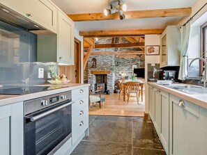 A modern kitchen with a stone fireplace, wooden beams, and a dining area with a stone floor. - 3 Bed in Padstow (oc-51214) (Padstow)