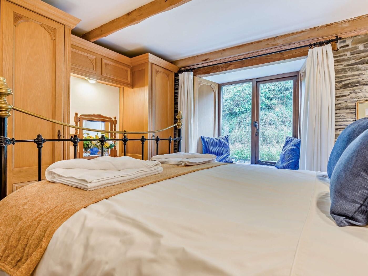 A hotel room with a large bed, wooden furniture, a stone wall, and a window with curtains.