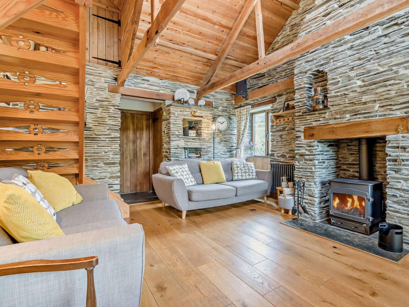 Une pièce chaleureuse avec un mur en pierre, des poutres apparentes, une cheminée, un canapé et un meuble en bois.