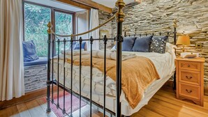 A bedroom with a stone wall, a metal bed frame, a wooden nightstand, and a window with curtains. - 3 Bed in Padstow (oc-51214) (Padstow)